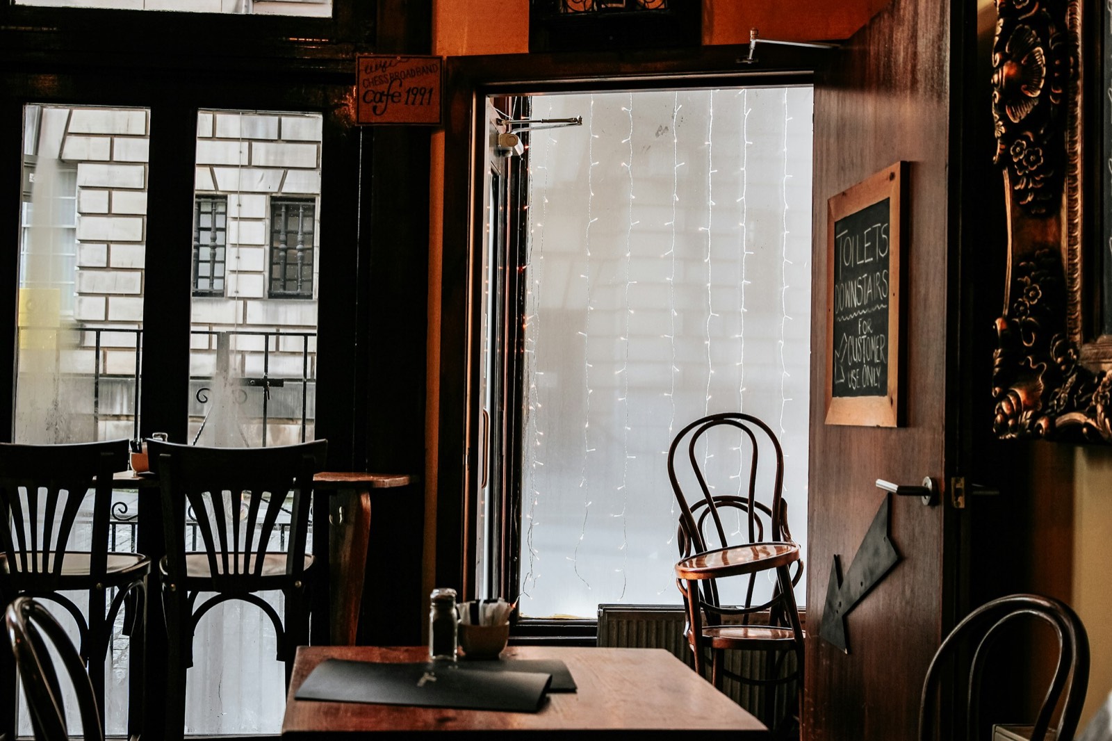 Empty tables and bentwood chairs by a window in a dark panelled bar.