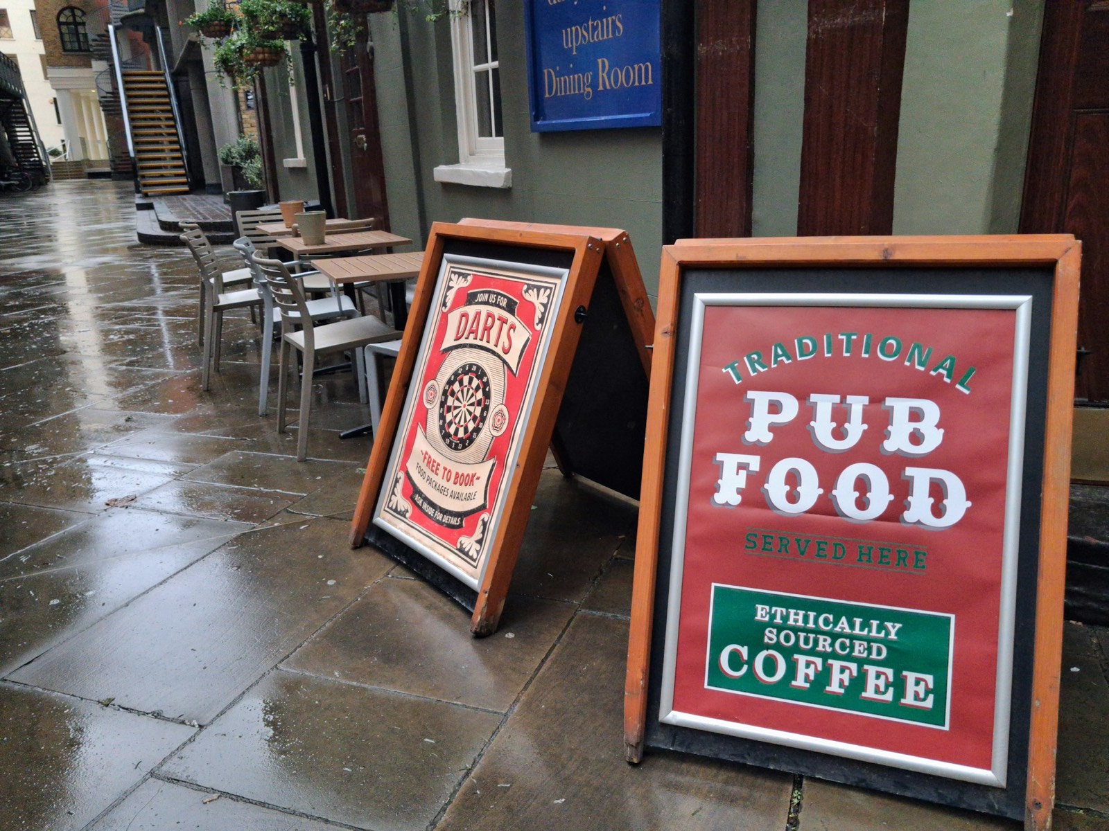A-frame pub signs on a wet pavement outside a traditional British pub.